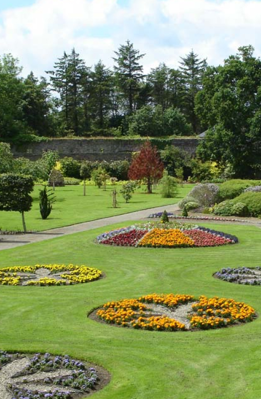 A vibrant view of Vandeleur Walled Garden & Visitor Centre, showcasing colorful flower beds bursting with blooms in shades of pink, yellow, orange, and purple.