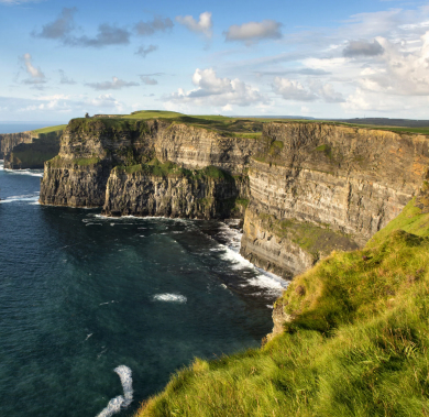 Magical view of the Cliffs of Moher towering over the Atlantic Ocean with waves crashing below on a summer day showing blue skies with minimal clouds.